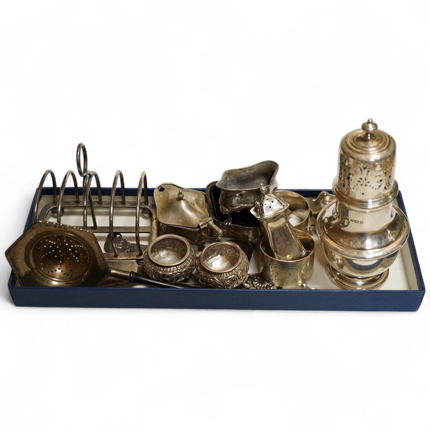 A George V silver sugar caster, Sheffield, 1914, Walker & Hall, together with a four division toast rack, a five peice Edwardian cruet set a/f, a pair of Indian Cutch salts, pair engraved napkin rings, Victorian fiddle,